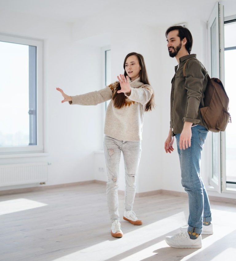 Femme montrant un espace vide à un homme, tous deux discutent dans un intérieur lumineux.