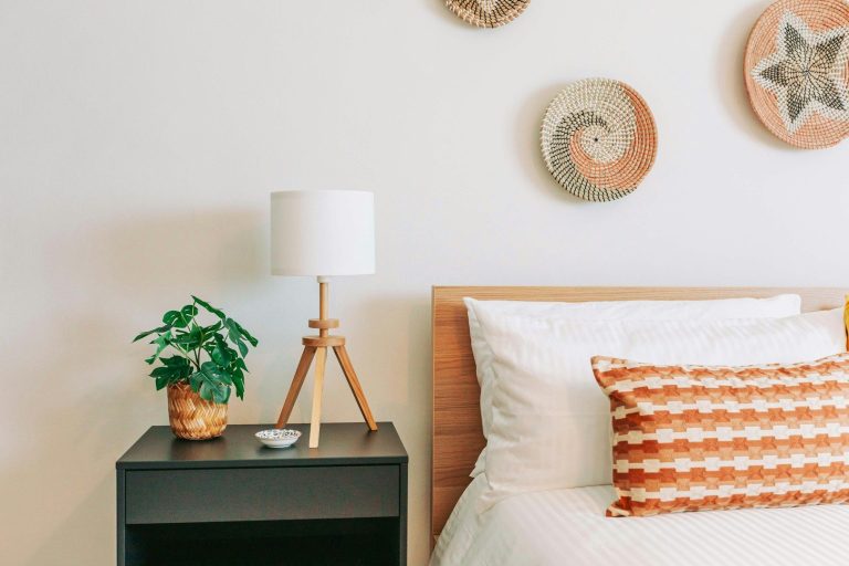 Chambre moderne avec lit, lampe, plante, et décor mural tressé.