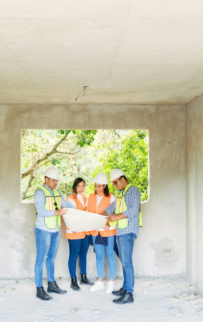 Visuel réunion chantier - Intësia Design Vertou Quatre personnes en sécurité discutent des plans de construction dans un bâtiment.