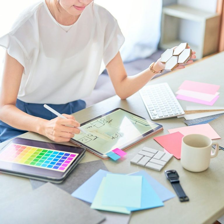 Femme travaillant sur une tablette avec des notes colorées et un mug de café sur une table.